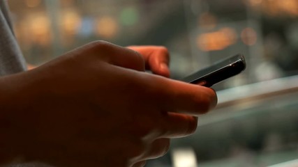 Close up shot of young man using smart phone for chatting with friends on the shopping centre background at night .