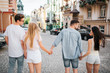 © estradaanton - Two couples are walking together down the street and holding each other's hands. Guy in jeans clothes is looking at brinette girl. Guy in glasses is talking to blonde girl.
