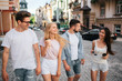 © estradaanton - Cheerful young people are walking down the street. Three of them are looking at chinese girl. She holding glasses and cup of coffee in hands. All of them are smiling.
