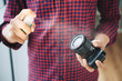 Faceless shot of casual man spraying lens of photo camera with special cleaning fluid to protect from dirt