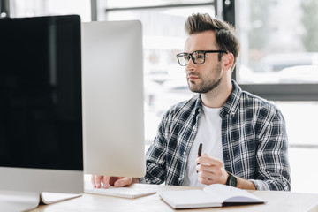 focused young man in eyeglasses working with desktop computer