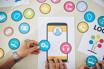Wall Mural - crop shot from above of coworkers choosing set of colorful paper icons while coworking on new smartp