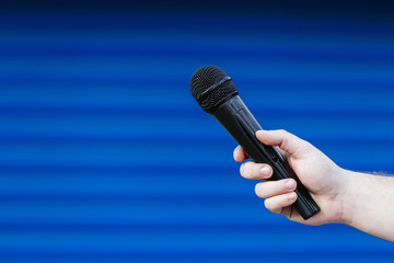 A man holds a microphone in a blue blurred background