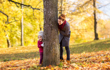 Family, Season And People Concept - Happy Mother And Little Daughter At Tree Trunk Playing In Autumn Park