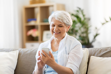 Wall Mural - technology, communication and people concept - happy senior woman with smartphone at home