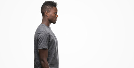 Sticker - Young african american man wearing grey t-shirt looking to side, relax profile pose with natural face with confident smile.