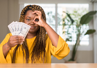 Canvas Print - African american woman holding dollars with happy face smiling doing ok sign with hand on eye looking through fingers