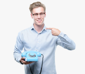 Sticker - Young handsome blond man holding vintage telephone with surprise face pointing finger to himself