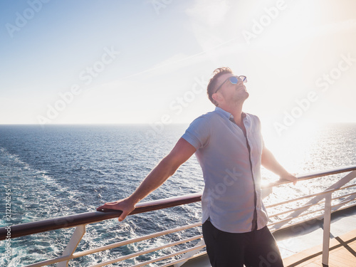 Fotografía Attractive man in sunglasses on the top deck of a cruise ship looking out into the distance against the background of a sunset