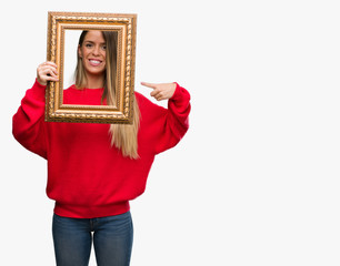 Wall Mural - Beautiful young woman holding vintage frame very happy pointing with hand and finger