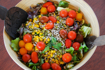 Fresh, healthy mixed salad bowl from top with lettuce, cherry tomatoes, corn and sunflower seeds. Wood cutlery set inside ready to serve