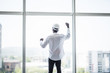 © dianagrytsku - Young afro american man in protective hemlet standing in front of panoramic windows with reaised hands of victory and sucess