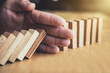 © Freedomz - Strategy and successful intervention concept for business, businessman hand Stopping Falling wooden Dominoes effect from continuous toppled or risk