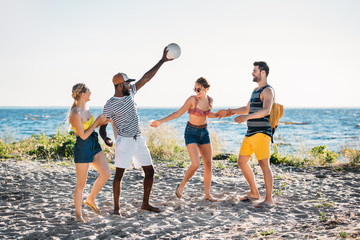 happy young multiethnic friends playing with ball on sandy beach