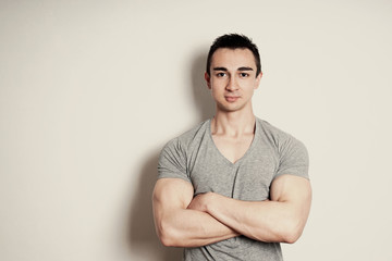 Wall Mural - muscular young man with arms crossed standing against wall with copy space. vintage filter effect.