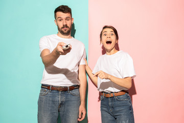 Wall Mural - Closeup portrait of young couple, man, woman. One being excited happy smiling, other serious, concerned, unhappy on pink and blue background. Emotion contrasts