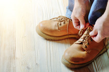 Carpenter In Blue Jeans Tying Shoelaces Of Yellow Work Boots On On Wooden Floor. Place For Text