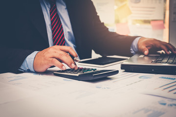 A businessman analyzing investment charts with using calculator for calculate of finance at workplace. Business concept.