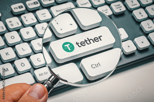 Fotografía magnifying glass in hand focused on computer key with tether coin logo