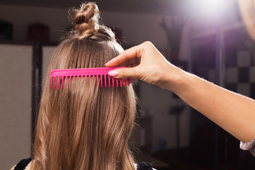 Wall Mural - professional hairdresser brushing hair of a young model using a pink brush in a beauty salon. concept of carefull hair treating