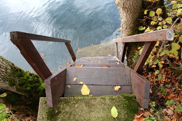 Wooden brown painted steps on river bank leading to small concrete platform currently under water with autumn fallen leaves surrounding it