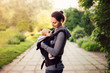 © troyanphoto - Little baby girl and her mother walking outside during sunset. Mother is holding and tickling her baby, babywearing in the ergo carrier