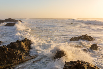 Wall Mural - Stormy waves crashing over rocky coast at sunset