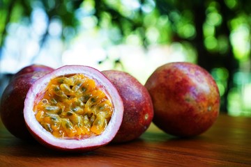 Wall Mural - Group of passion fruit with half cut on wooden table with blur green garden background, copy space, healthy food concept