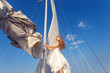 © khosrork - portrait of happy toothy smiley pretty girl with white dress and long curly blonde hair standing on yacht at summertime and blue sky. down view. looking away and standing near sail