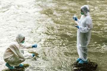 Two scientists in protective suits taking water samples from the river