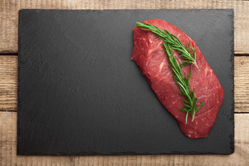 fresh raw meat with rosemary on black slate, on dark background, steak Ribeye