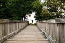 A Little Girl Reaches The End Of A Long Bridge And Celebrates In A Backlit Gap Through The Trees