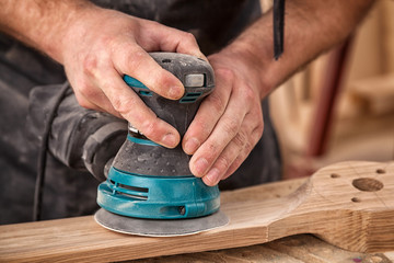 Close up of an young man builder carpenter equals polishes wooden board with a  random orbit sander  in the workshop