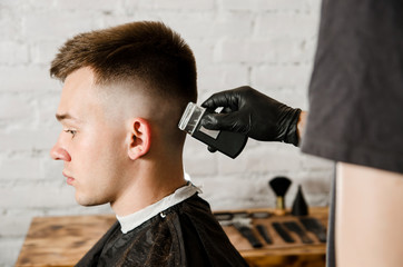 Barber does hair cut young guy on a brick wall background.