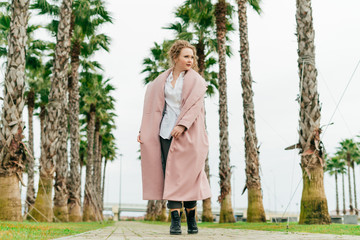 stylish curly woman in a long pink coat enjoying the warm spring weather in the park