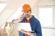 © gzorgz - Handsome handyman making call. Young repairman using laptop and mobile phone while standing at renovation area.