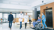 © Gorodenkoff - First Floor of the Busy Hospital, Doctors, Nurses and Personnel Busy Working, Assistant Moves Elderly Man in the Wheelchair. New Modern Medical Hospital with Professional Staff.