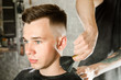 © vika33 - The hairdresser cleans the neck of a young guy with a brush with talc after a haircut against a brick wall background