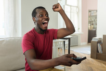 Horizontal Photo Of African American Man Dressed In Bright Red T-shirt Watching Sport Match On Television And Supporting His Favorite Team, Shouting, Cheering, Feeling Excited, Celebrating Goal