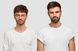 © WHstudio Leushin N - Indoor shot of serious two Caucasian men look directly at camera, wear casual clothes, have stubbles, work as friendly team, stand against white background. People, facial expressions concept