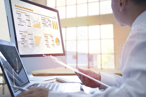 Cuadros en Lienzo Businessman analysing on business performance on desktop and notebook computer with orange-gold graphs