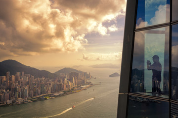 Wall Mural - Young man traveler take a photo of Hong Kong City skyline at sunset  from sky 100 Hongkong.