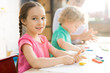 © Seventyfour - Warm toned portrait of cute little girl smiling at camera while sitting at table in art and craft lesson of development school, copy space