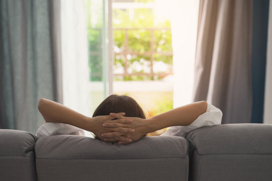 young woman relaxing on sofa at cozy home and looking outside in living room