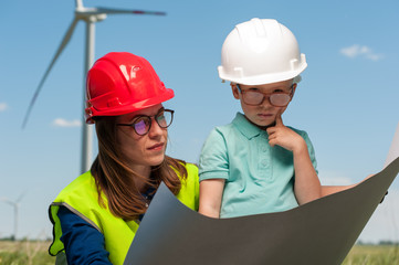 Charming young woman engineer windmills in a red helmet and green vest shows his young son a project plan