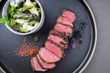 Modern barbecue dry aged sliced fillet steak spring salad with and green and white asparagus as closeup on a plate