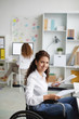 © pressmaster - Happy businesswoman in wheelchair looking at camera while working with financial papers in office