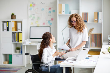 Wall Mural - Two young confident businesswomen discussing documents and ideas at meeting by workplace