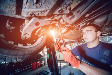 Wall Mural - Car mechanic examining car suspension of lifted automobile at repair service station