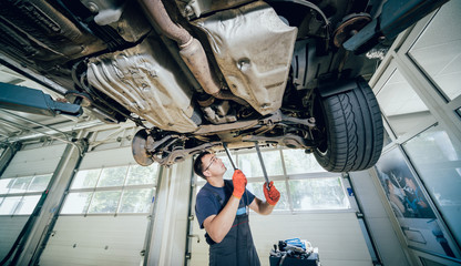 Wall Mural - Car mechanic examining car suspension of lifted automobile at repair service station